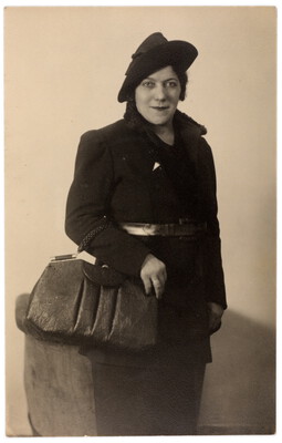 Frau sitzend mit Hut und grosser Tasche